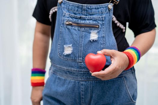 Asian lady wearing rainbow flag wristbands and hold red heart, symbol of LGBT pride month celebrate annual in June social of gay, lesbian, bisexual, transgender, human rights.