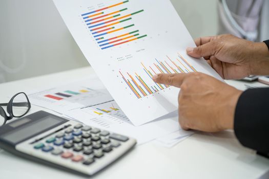 Asian accountant working and analyzing financial reports project accounting with chart graph and calculator in modern office, finance and business concept.