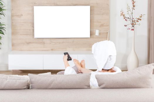Woman sitting on couch with towel on her head watching tv. White screen for design
