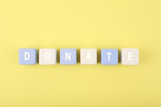 Donation concept on pastel yellow background. Donate word on blue and white cubes