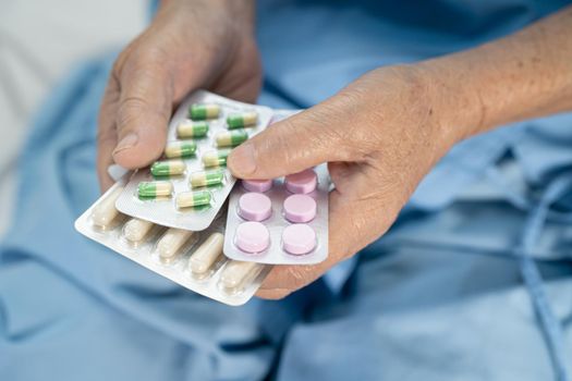 Asian senior or elderly old lady woman patient holding antibiotics capsule pills in blister packaging for treatment infection patient in hospital; Pharmacy drugstore concept.