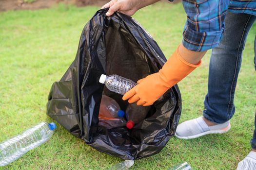 Asian woman volunteer carry water plastic bottles into garbage bag trash in park, recycle waste environment ecology concept.