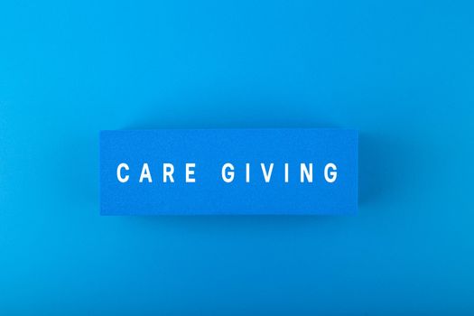 Care giving text written on blue rectangular against blue background with light gradient. Minimal concept of charity, donation and care giving in monochromatic blue colors