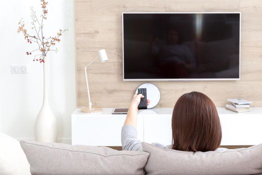 Young woman watching TV in living room, back view