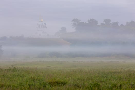foggy summer morning landscape with the church on the hill in the background.