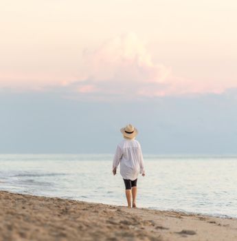 Woman wearing straw hat walking on beach at sunset
