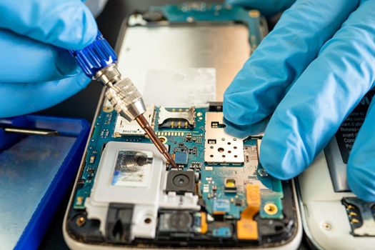 Technician repairing inside of mobile phone by soldering iron. Integrated Circuit. the concept of data, hardware, technology.