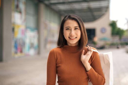 Portrait of cheerful young Asian woman with shopping bags at outdoor mall