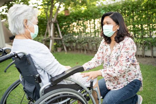 Help Asian senior or elderly old lady woman on wheelchair and wearing a face mask for protect safety infection Covid-19 Coronavirus in park.