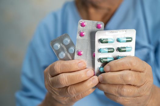 Asian senior or elderly old lady woman patient holding antibiotics capsule pills in blister packaging for treatment infection