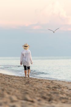 Woman wearing straw hat walking on beach at sunset