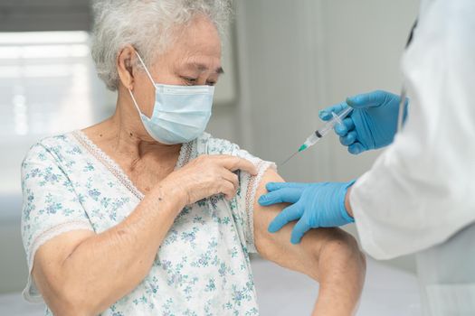 Elderly Asian senior woman wearing face mask getting covid-19 or coronavirus vaccine by doctor make injection.