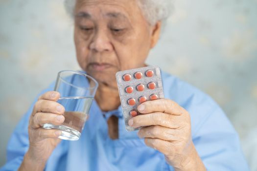 Asian senior or elderly old lady woman patient holding antibiotics capsule pills in blister packaging for treatment infection patient in hospital, Pharmacy drugstore concept.