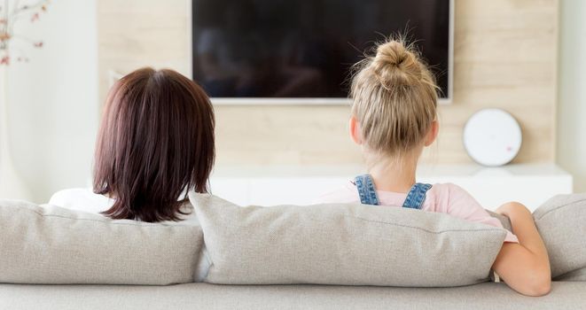 Mother and daughter sitting on a sofa at their home and watching tv, Family time