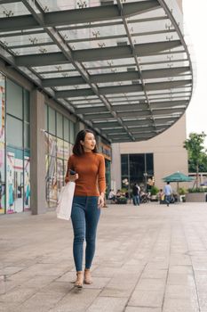 Young happy Asian woman with shopping bags walking on street.