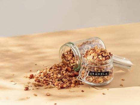 Homemade granola sprinkled of glass jar over pastel beige background. Aesthetic oat granola, beautiful shadows, champagne yellow background. Healthy breakfast concept