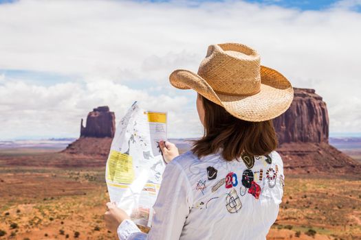 Back side of girl wearing straw hat searching right direction on map in Monument Valley, Utah, USA