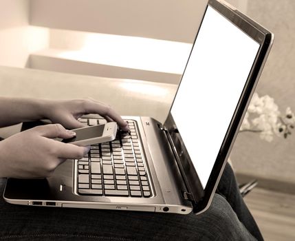 Woman using laptop and telephone while sitting on a couch