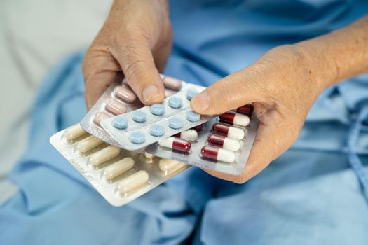 Asian senior or elderly old lady woman patient holding antibiotics capsule pills in blister packaging for treatment infection patient in hospital; Pharmacy drugstore concept.