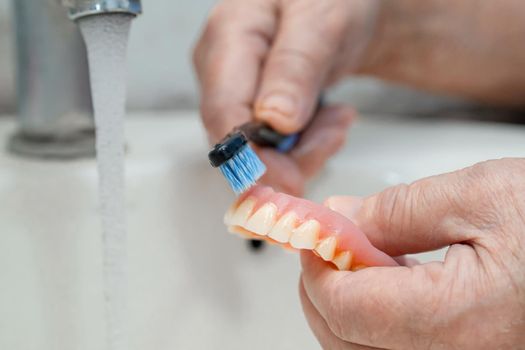 Asian senior or elderly old woman patient use toothbrush to clean partial denture of replacement teeth.