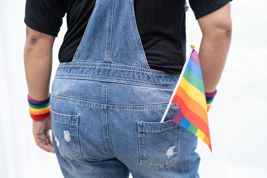 Asian lady wearing blue jean jacket or denim shirt and holding rainbow color flag, symbol of LGBT pride month celebrate annual in June social of gay, lesbian, bisexual, transgender, human rights.