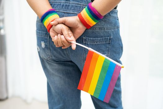 Asian lady wearing blue jean jacket or denim shirt and holding rainbow color flag, symbol of LGBT pride month celebrate annual in June social of gay, lesbian, bisexual, transgender, human rights.