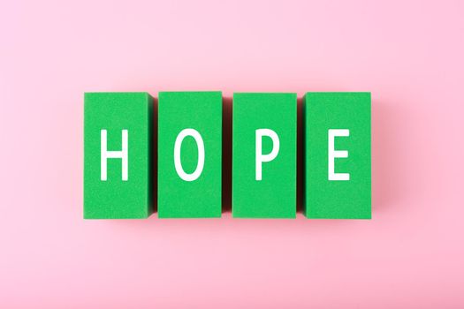 Concept of hope and faith. Minimal flat lay with hope single word written on green blocks against bright pink background. 