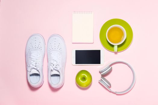 Healthy lifestyle concept. Sneakers, tea, apple and headphone on pastel color background.