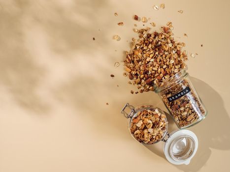 Homemade granola sprinkled of glass jar over pastel beige background. Top view or flat lay. Aesthetic oat granola, beautiful shadows, champagne yellow background. Healthy breakfast concept