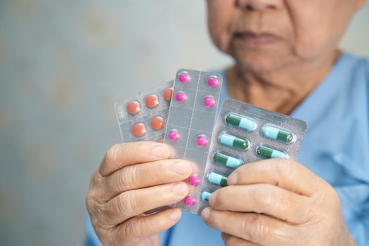 Asian senior or elderly old lady woman patient holding antibiotics capsule pills in blister packaging for treatment infection patient in hospital; Pharmacy drugstore concept.