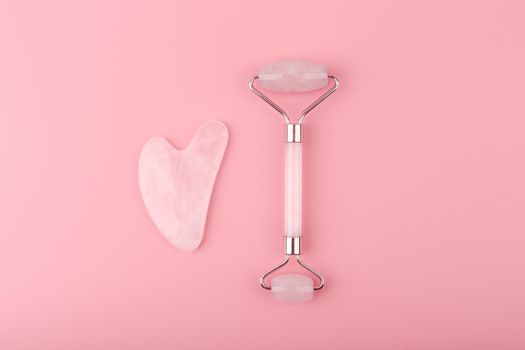 Jade roller and heart shaped guasha scraper massager made of pink quartz on pink background. Concept of self treatment and facial guasha massage for skin lifting and toning