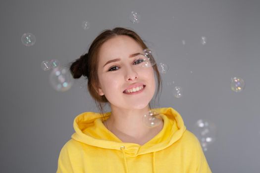 portrait of charming young woman in yellow among soap bubbles on bright grey background. fashionable teenager. trendy colours