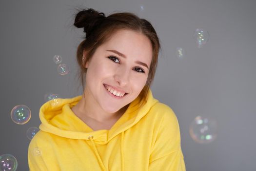 woman in yellow among soap bubbles on grey background.