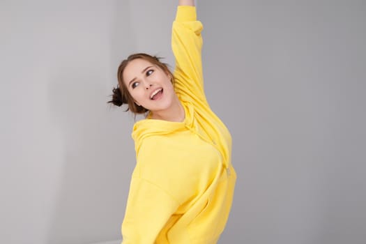 cheerful positive brunette woman in yellow hoodie in white bedroom on bed with white linens. happy people. millennial generation. fashionable teenager.