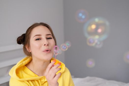 portrait of charming young woman in yellow among soap bubbles on bright grey background. fashionable teenager. trendy colours