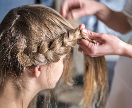 Hairdresser makes braid in beauty salon