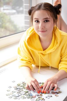 pretty brunette girl in yellow hoodie arranging pieces of a Jigsaw Puzzle Game in bright white room. playing board game home