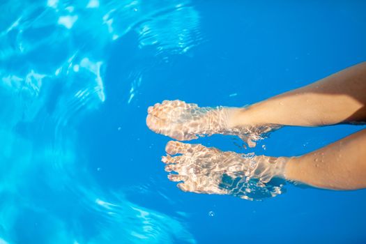 Summer vacation concept. The legs of a young woman on the background of the blue water of the pool. Swimming in the pool. Relaxation, sunbathing and joy.