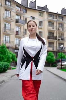 confident brunette woman in red pants and white blouse and jacket walking in the street.