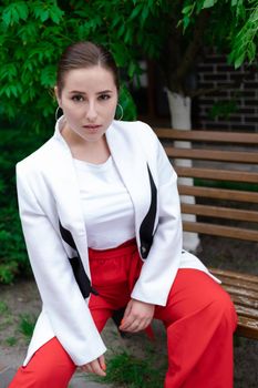 sexy confident brunette woman in red and white outdoors sitting on bench.