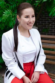 charming young brunette woman in red and white posing outdoors. summertime, green trees.