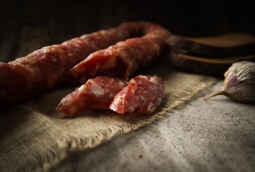 Sausage and rye sliced bread on natural linen napkin and garlic clove on rustic wooden background