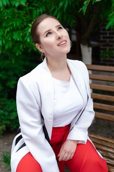 sexy confident brunette woman in red and white outdoors sitting on bench.