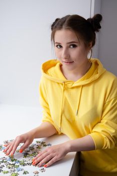 pretty brunette girl in yellow hoodie arranging pieces of a Jigsaw Puzzle Game in bright white room. playing board game home