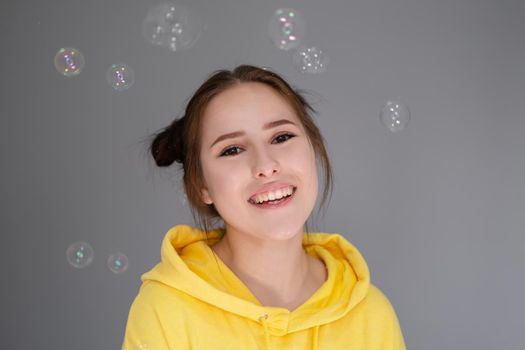 portrait of charming young woman in yellow among soap bubbles on bright grey background. fashionable teenager. trendy colours