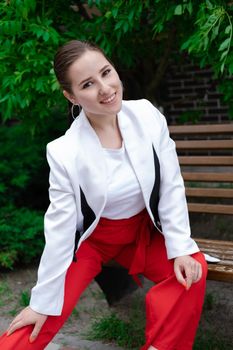 sexy confident brunette woman in red and white outdoors sitting on bench.