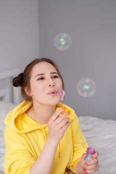 portrait of charming young woman in yellow among soap bubbles on bright grey background. fashionable teenager. trendy colours