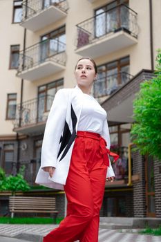 confident brunette woman in red pants and white blouse and jacket walking in the street.