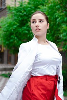 confident brunette woman in red pants and white blouse and jacket walking in the street.