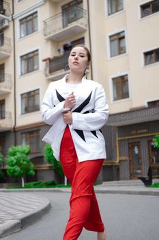 confident brunette woman in red pants and white blouse and jacket walking in the street.